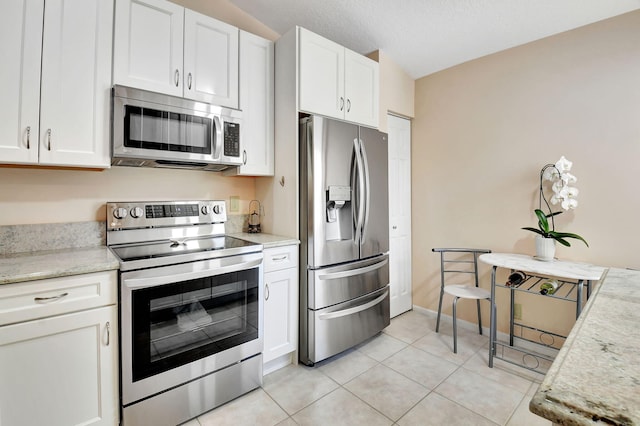 kitchen featuring stainless steel appliances, white cabinetry, vaulted ceiling, light tile patterned flooring, and light stone countertops