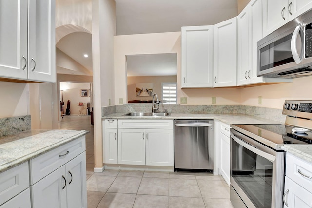 kitchen featuring appliances with stainless steel finishes, a sink, light tile patterned floors, white cabinets, and light stone counters