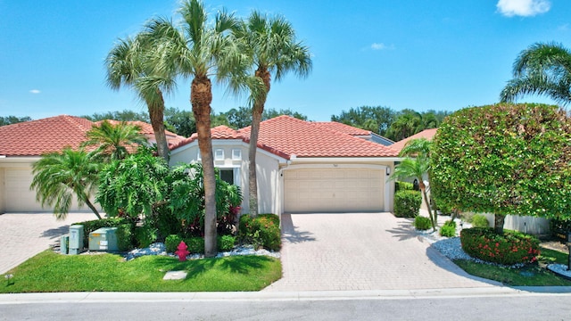 mediterranean / spanish-style house with stucco siding, an attached garage, a tile roof, and decorative driveway