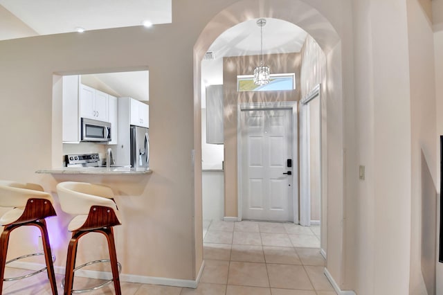 entrance foyer featuring baseboards, arched walkways, light tile patterned flooring, and a chandelier