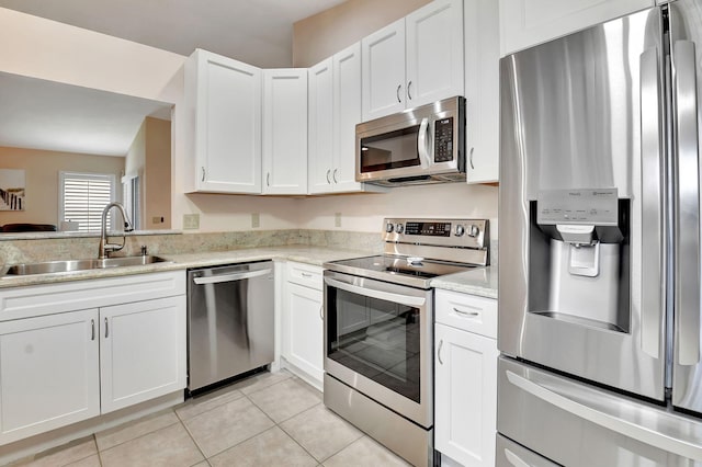 kitchen featuring appliances with stainless steel finishes, a sink, light tile patterned floors, white cabinetry, and light stone counters