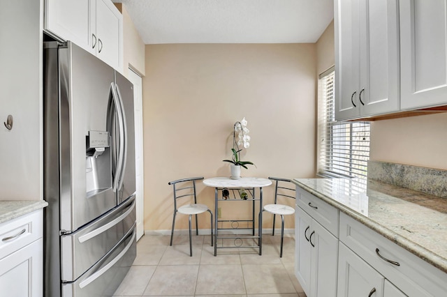 kitchen with stainless steel refrigerator with ice dispenser, light tile patterned floors, light stone counters, white cabinetry, and baseboards