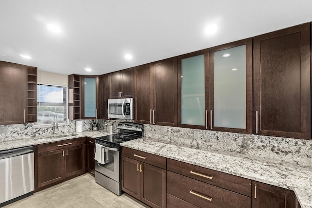 kitchen with dark brown cabinetry, stainless steel appliances, light stone counters, and a sink