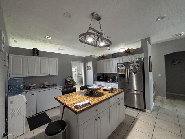 7746 99th Ct, Vero Beach, FL 32967 - kitchen with stainless steel refrigerator with ice dispenser, arched walkways, light tile patterned floors, white cabinets, and butcher block countertops