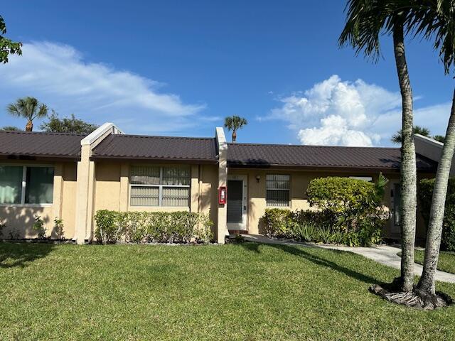 ranch-style house with a front lawn, stucco siding, and metal roof