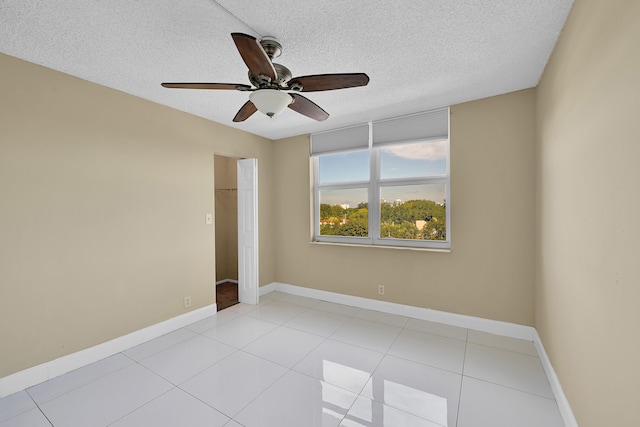 unfurnished room with a ceiling fan, a textured ceiling, light tile patterned flooring, and baseboards