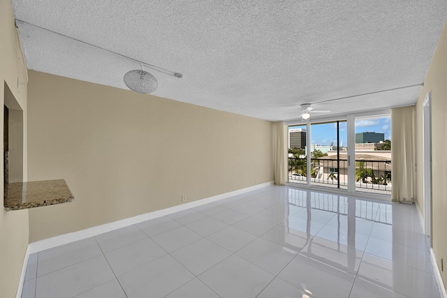 unfurnished room featuring a textured ceiling, baseboards, a ceiling fan, and light tile patterned flooring