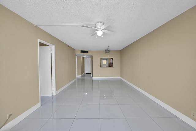 tiled empty room featuring a textured ceiling, ceiling fan, visible vents, and baseboards