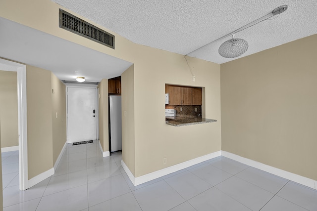 interior space featuring visible vents, baseboards, a textured ceiling, and light tile patterned floors