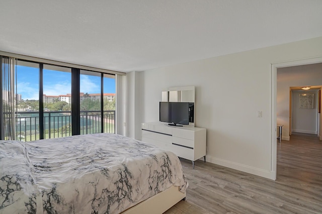 bedroom featuring access to outside, baseboards, a wall of windows, and light wood-style flooring