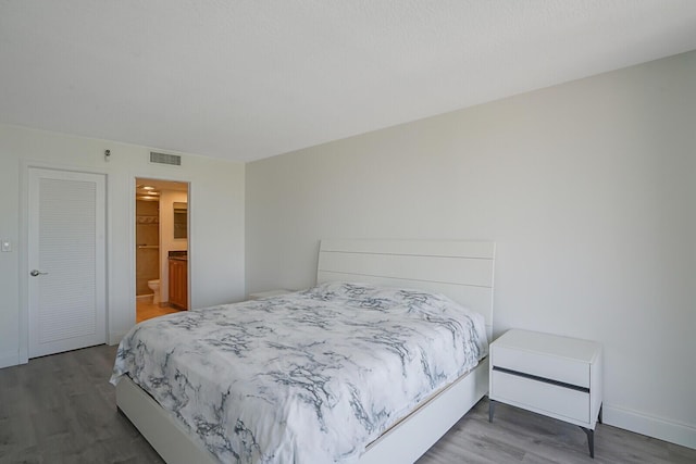 bedroom with baseboards, visible vents, and wood finished floors