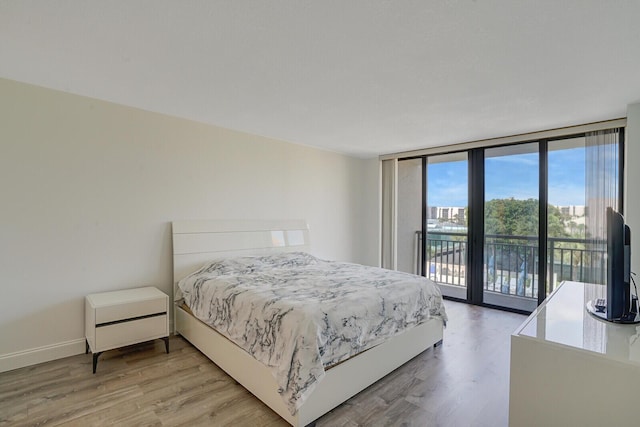 bedroom featuring baseboards, floor to ceiling windows, access to exterior, and light wood-type flooring