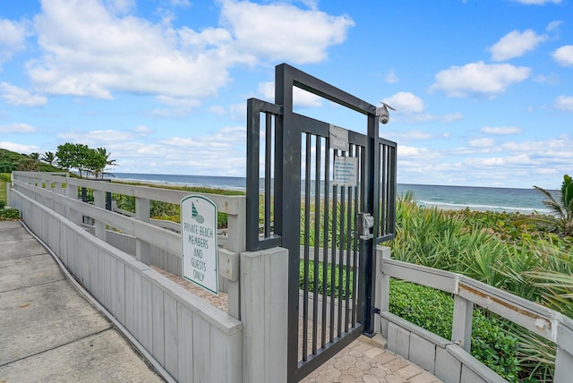 view of gate featuring a beach view, a water view, and fence