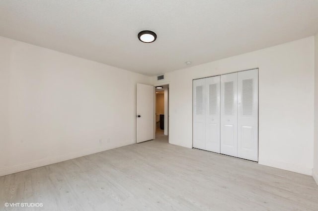unfurnished bedroom featuring a closet, baseboards, visible vents, and wood finished floors
