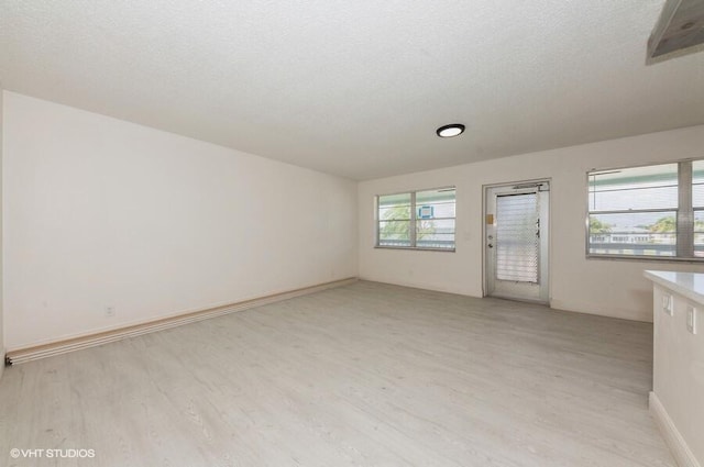 unfurnished living room featuring light wood-style floors, baseboards, and a textured ceiling