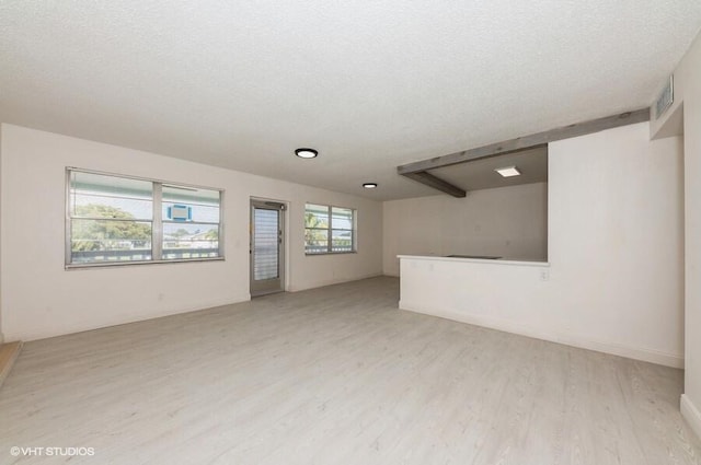 empty room with a textured ceiling, light wood-style flooring, and baseboards