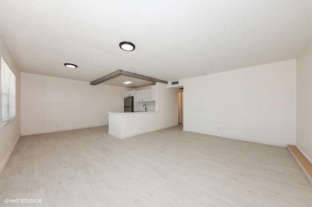 unfurnished living room with light wood-type flooring, visible vents, baseboards, and a sink