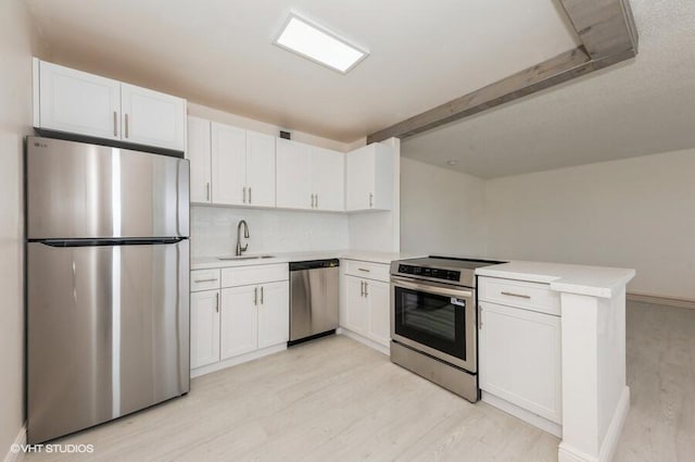 kitchen featuring appliances with stainless steel finishes, a sink, a peninsula, light countertops, and light wood-type flooring