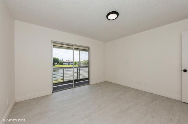 empty room with baseboards, light wood-type flooring, and a textured ceiling