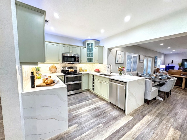 380 Laurie Rd, West Palm Beach, FL 33405 - kitchen with appliances with stainless steel finishes, a sink, light wood finished floors, green cabinetry, and decorative backsplash