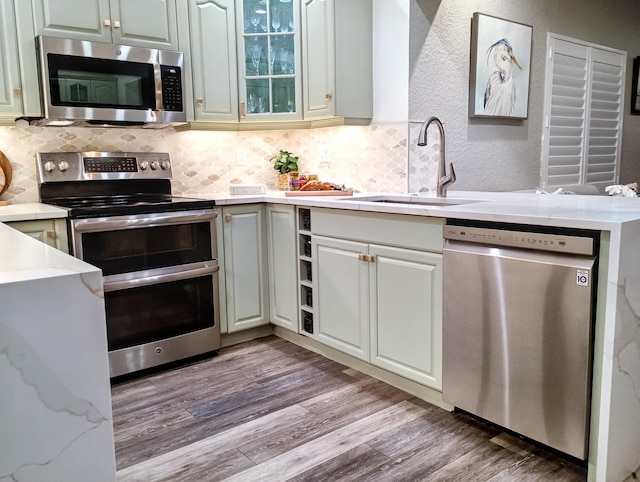 kitchen featuring a sink, backsplash, light wood-style floors, appliances with stainless steel finishes, and a textured wall