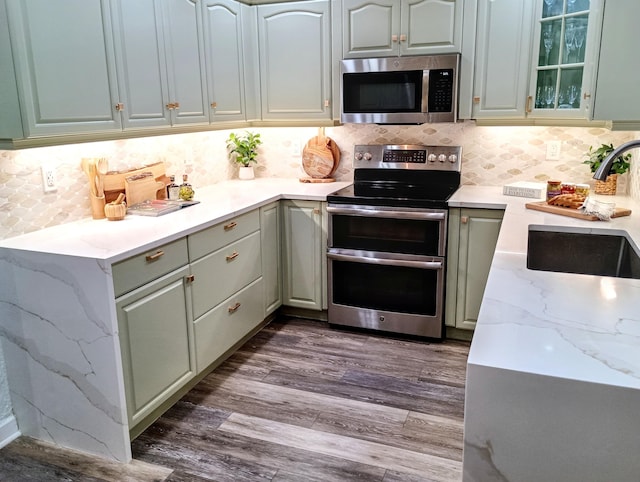 kitchen featuring a sink, stainless steel appliances, light stone counters, dark wood-type flooring, and backsplash