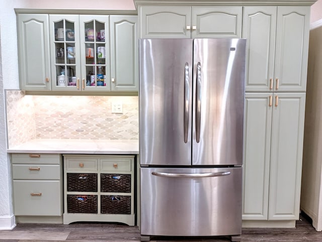 kitchen featuring freestanding refrigerator, decorative backsplash, glass insert cabinets, and wood finished floors