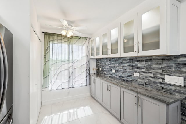kitchen featuring decorative backsplash, ceiling fan, stone countertops, freestanding refrigerator, and white cabinetry