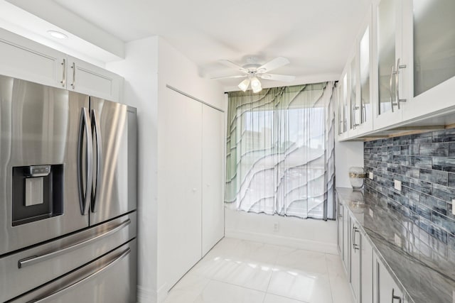 kitchen with ceiling fan, dark stone counters, decorative backsplash, stainless steel refrigerator with ice dispenser, and glass insert cabinets