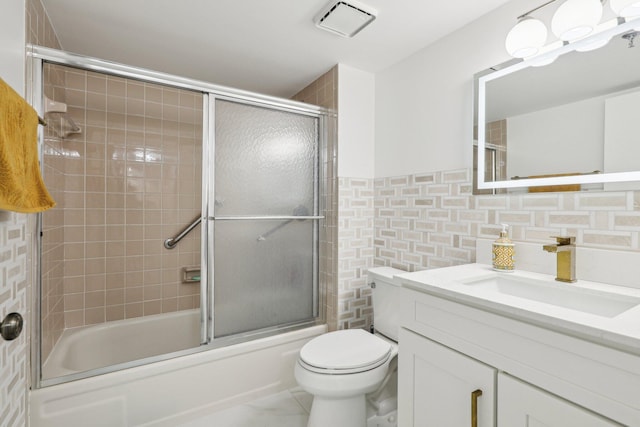full bath with visible vents, tile walls, bath / shower combo with glass door, vanity, and toilet