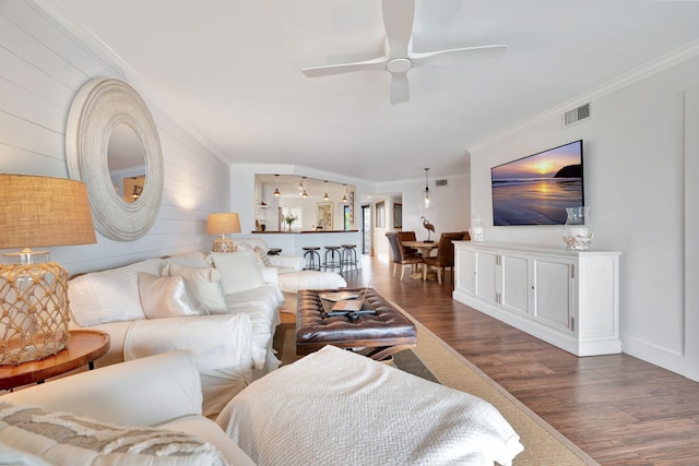 living area with ceiling fan, visible vents, ornamental molding, and wood finished floors