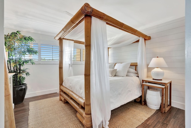 bedroom with crown molding, wood walls, dark wood-style flooring, and baseboards