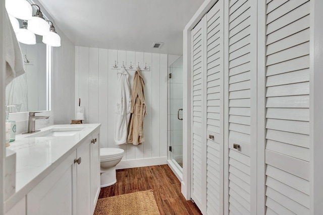 full bath featuring a closet, wood finished floors, toilet, and a shower stall