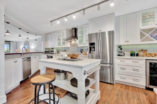 kitchen with wall chimney range hood, appliances with stainless steel finishes, tasteful backsplash, a sink, and wine cooler