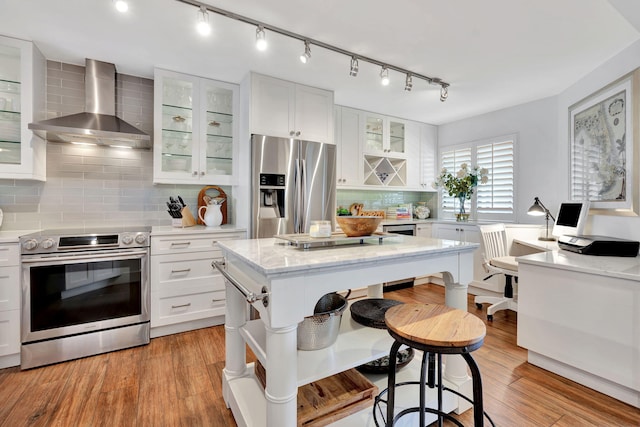kitchen with decorative backsplash, wall chimney exhaust hood, white cabinets, light wood finished floors, and stainless steel appliances