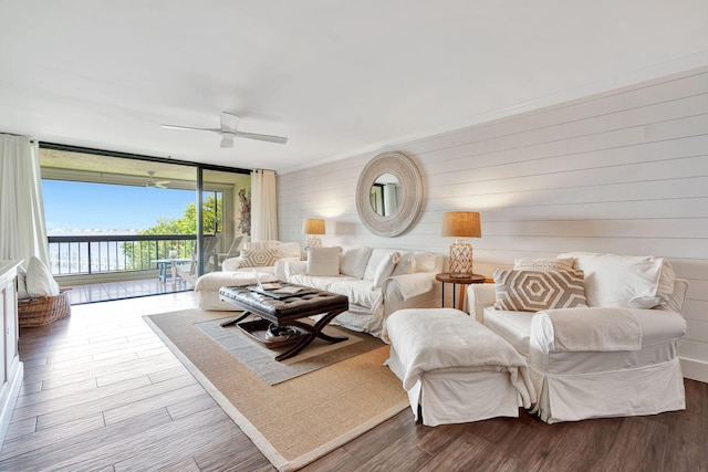 living room with ceiling fan, a wall of windows, wood walls, and wood finished floors