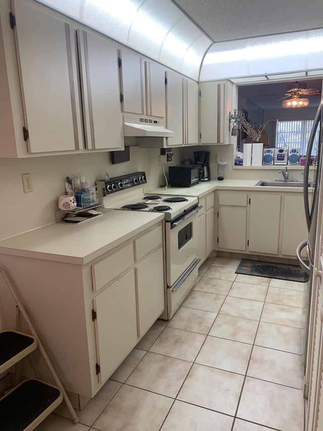 kitchen featuring a sink, under cabinet range hood, light countertops, light tile patterned floors, and white range with electric stovetop