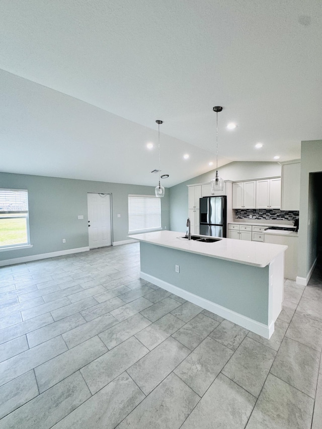 kitchen featuring lofted ceiling, stainless steel refrigerator with ice dispenser, white cabinets, tasteful backsplash, and a sink
