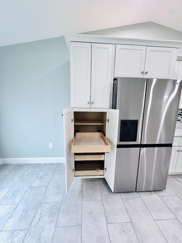 kitchen featuring stainless steel refrigerator with ice dispenser, baseboards, lofted ceiling, and white cabinets