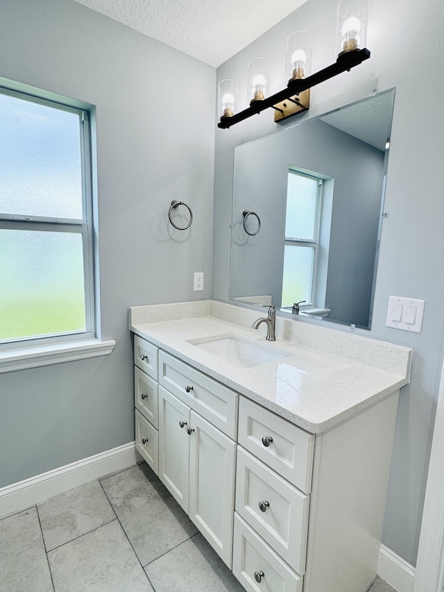 bathroom featuring baseboards, a textured ceiling, a healthy amount of sunlight, and vanity
