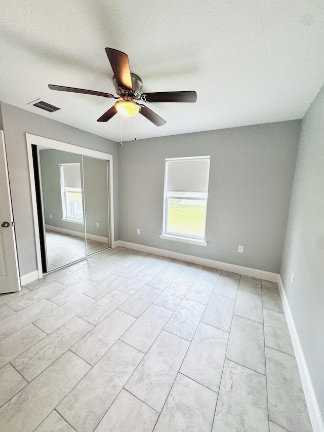 unfurnished bedroom with baseboards, visible vents, multiple windows, and a closet