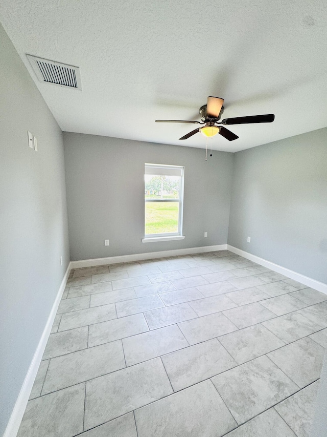 empty room with light tile patterned flooring, a textured ceiling, a ceiling fan, baseboards, and visible vents