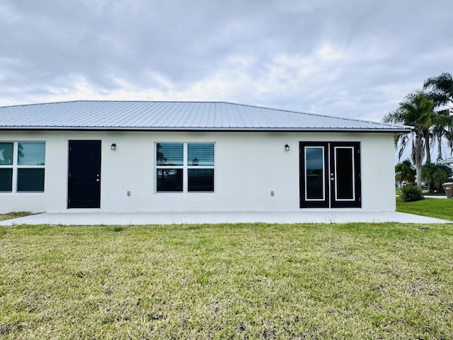 back of property with a lawn, stucco siding, and metal roof
