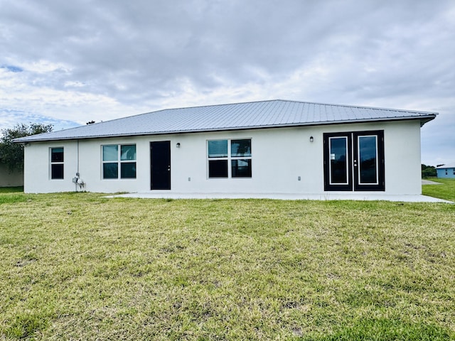 back of property with a yard, metal roof, and stucco siding