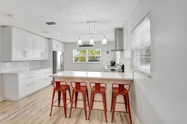 124 Mockingbird Ln Unit 124, Delray Beach, FL 33445 - kitchen featuring island range hood, freestanding refrigerator, light wood-style flooring, decorative backsplash, and a textured ceiling
