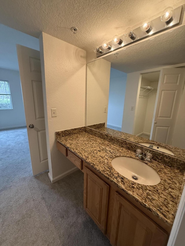 full bathroom with vanity, a textured ceiling, and baseboards