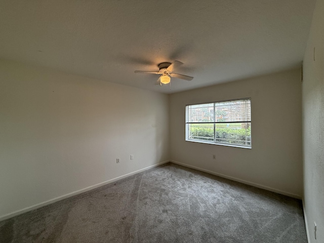 carpeted spare room featuring baseboards and a ceiling fan