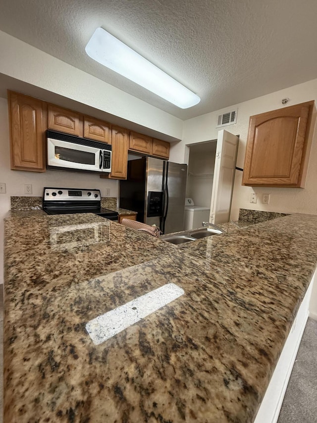 kitchen with appliances with stainless steel finishes, a sink, a textured ceiling, a peninsula, and visible vents