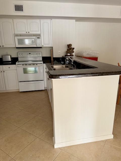 242 Village Blvd Unit 2203, Tequesta, FL 33469 - kitchen with white appliances, dark countertops, light tile patterned floors, and a peninsula