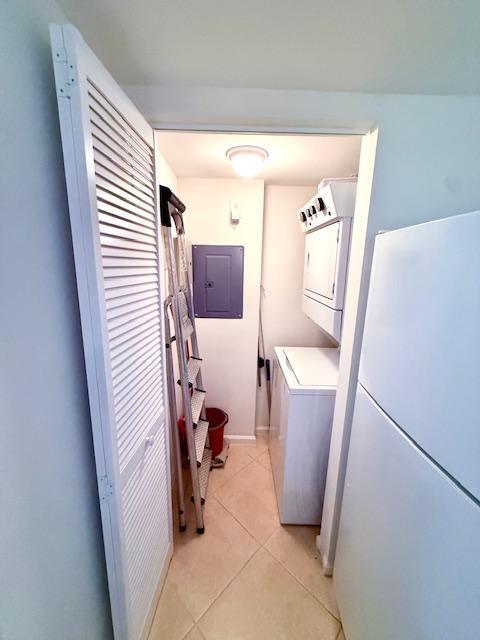 clothes washing area featuring electric panel, stacked washing maching and dryer, light tile patterned flooring, and laundry area